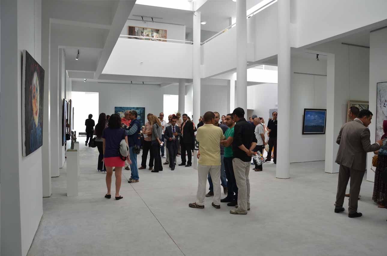 Group of people attending an art exhibition in a modern gallery with white walls and displayed artworks.