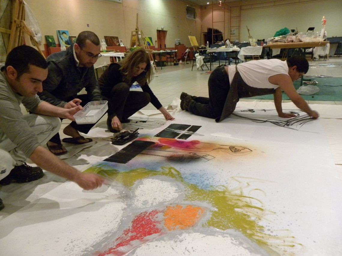 Group of people working on a collaborative abstract painting spread on the floor in a spacious art workshop.